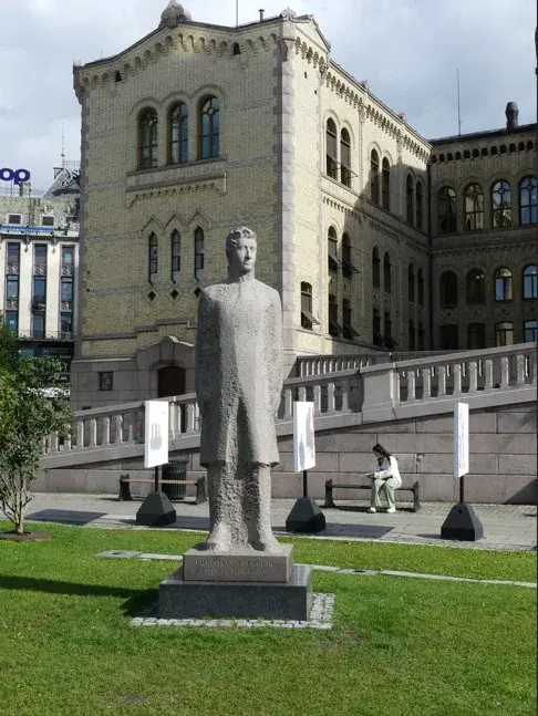 Henrik Ibsen i granitt på sokkel på plenen foran Stortingsbygningen i Oslo
