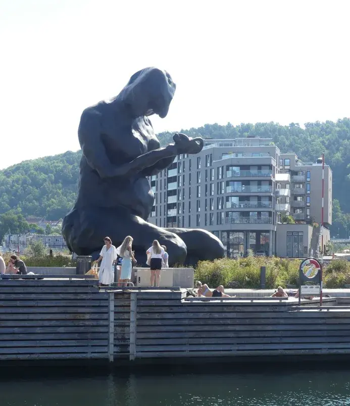 Mother, den store mørke bronsefiguren på kne ved Bjørvika, med mennesker på bryggekanten nedenfor